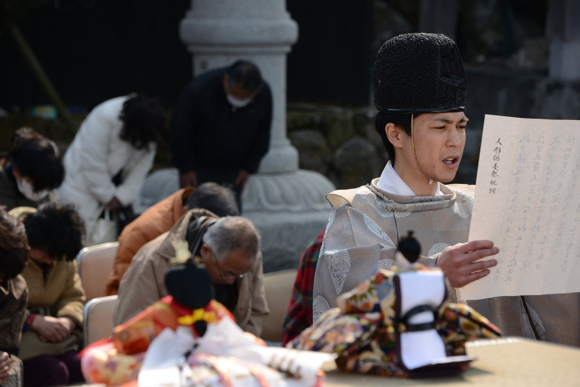 人形を前に祝詞を奏上する神職と、祈りを捧げる参列者